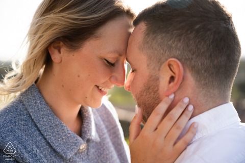 Provencal Sun-kissed Embrace: A Grignan Engagement Portrait of Love A couple sits face to face in Grignan, Drôme provençale, their expressions tender and loving. The sun backlights them, creating a warm, intimate atmosphere in this close-up engagement portrait.