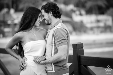 A newly engaged couple stands head to head, smiling warmly, on the Marbella Club Pier. The black and white photo highlights their joy during their engagement portrait session.