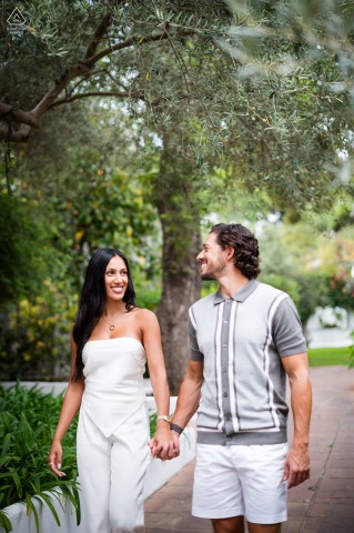 A couple walks hand in hand through a park near Marbella Club Pier, surrounded by lush greenery. The vertical portrait highlights their connection during this photo session.