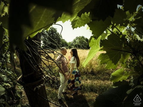 A couple stands face to face in Ceparana, framed by lush vineyard foliage. Their gentle expressions and close pose capture the romance of their engagement portrait.