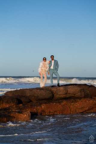 Coastal Elegance: A Punta del Este Engagement on the Rocks A stylish, elegantly dressed couple poses on rocky outcrops at the beach in Punta del Este, Uruguay. The dramatic coastal scenery highlights their sophistication during their engagement photos.