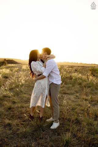 Buenos Aires Sunset: A Sunlit Kiss to Forever's Beginning A couple kisses in a sunlit field in Provincia de Buenos Aires, Argentina, during their engagement photo shoot. The sunlight bursts behind them, casting a warm, romantic glow over the scene.