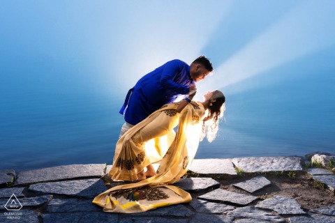 A couple dances at Lake Louise, Canada, standing on stone pavers at a scenic lookout. The backlighting highlights their joyful expressions as he gently dips her, framed by the lake’s beauty.