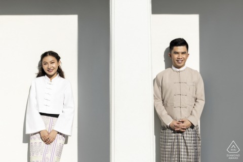 A couple stands apart with shoulders square to the camera in a minimalistic, modern setting in Bangkok, Thailand. The clean background emphasizes their elegant, contemporary style during their engagement portrait session.