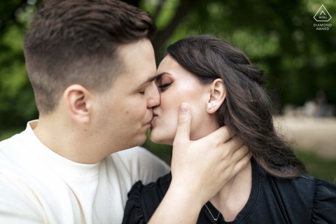 In Hármashatárhegy, Hungary, a couple shares a tender kiss in a romantic close-up. The background features softly focused greenery, highlighting the intimacy and emotion of their engagement portrait.