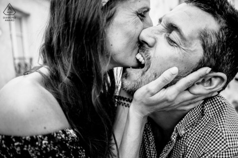 In Paris, France, a couple shares a playful kiss as he gently bites her chin. The black and white close-up captures their affection and fun loving connection in an intimate portrait.