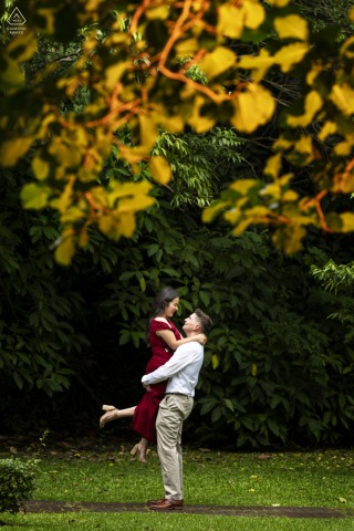 At Hotel Bougainvillea in Santo Domingo, Heredia, Costa Rica, a man lifts his partner joyfully as colorful fall foliage in the trees overhead naturally frames the couple during their engagement portrait session.