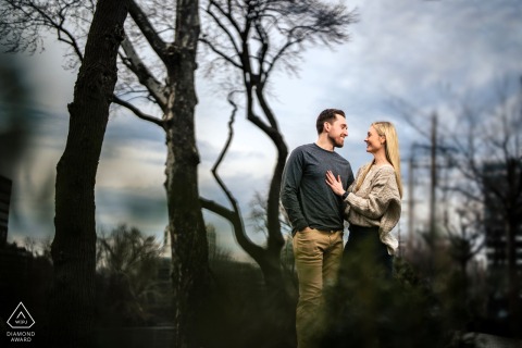 Warm Connection Illuminated Outdoors On Chilly Day At Conshohocken Trailhead Engagement Portrait At Conshohocken Trailhead in Philadelphia, a couple poses together outdoors on a chilly day. Thoughtful lighting highlights their expressions, conveying a sense of warmth and connection during their engagement portrait session.
