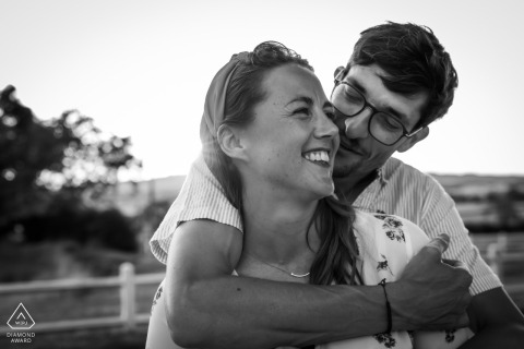 In Morvan, a couple shares a joyful laugh in a tight black and white portrait. He hugs her from behind, and both are smiling warmly, capturing their playful affection and happiness.