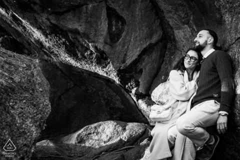 Intimate Black And White Portrait: Couple Sheltered Beneath Les Rochers du Carnaval Rocks At Les Rochers du Carnaval, a couple relaxes together sheltered beneath the rocks in a black and white portrait. Their comfortable pose highlights a sense of intimacy and ease in the natural setting.