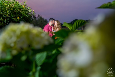 Romantic Pre-Wedding Portrait: Couple Embraced Among Garden Greenery And Blossoming Flowers, Spain Pre-wedding portrait in Spain: a couple poses among lush greenery and flowers in a garden.