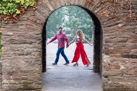 Pre-wedding portrait of a couple walking passed a stone archway in Lugo, Galicia, Spain.