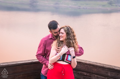 In Lugo, Galicia, Spain, a couple poses for a pre-wedding portrait with symmetrical framing. He embraces her from behind as they both face the camera, standing centered and connected in the composition.