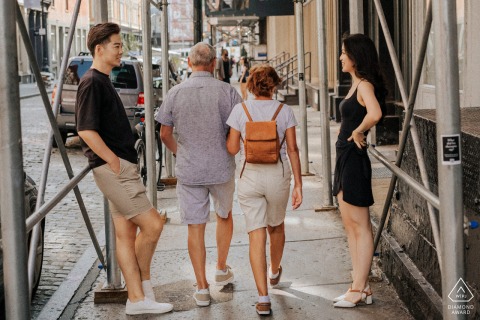 NYC engagement photography: Candid portrait in Central Park under scaffolding. Couple is the focus, with pedestrians adding a dynamic urban background.