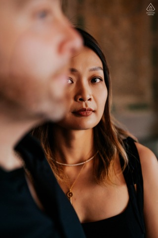 An intimate engagement portrait set in Central Park, where the woman's clear, direct gaze connects with the viewer from behind the softly framed profile of her partner.