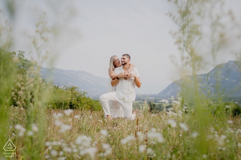 Engaged couple portrait in a field of flowers in Saint Jean de Moirans, France. Soft, out-of-focus green foliage creates a natural frame, highlighting the subjects amidst the blooms. 