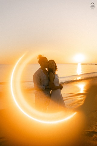 Les Sables d'Olonne Sunset Embrace: Backlit Engagement Portrait, "Ring Of Fire" Effect A backlit engagement portrait of a couple embracing on the beach at Les Sables d'Olonne, France. The sunset creates a powerful "ring of fire" effect, dramatically outlining their figures against the sky.