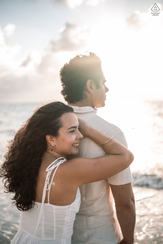 A pre-wedding couple stands near the tranquil water on Ipioca Beach. The subjects are facing the ocean, enjoying a quiet embrace against the picturesque backdrop of the unspoiled Brazilian shore.