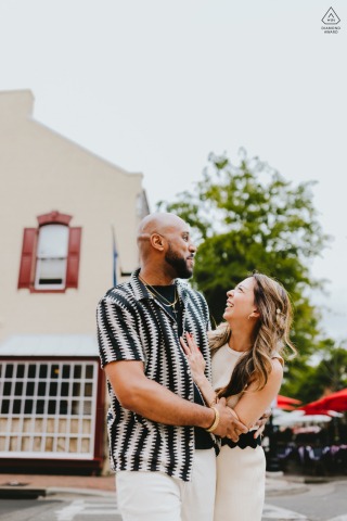 This tall vertical image captures a joyful couple in Old Town Alexandria, VA, standing on the street and looking at each other, captured mid-conversation while talking and laughing with genuine happiness.