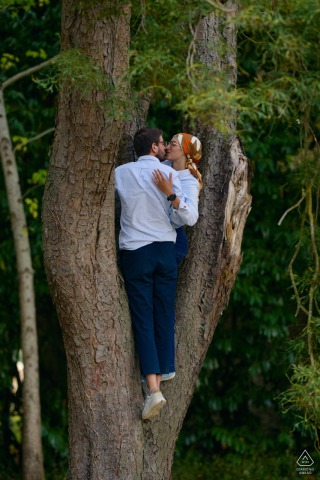 This playful Pays de la Loire portrait captures the adventurous couple after they have climbed a tree, standing together intimately within the natural V of the trunk.