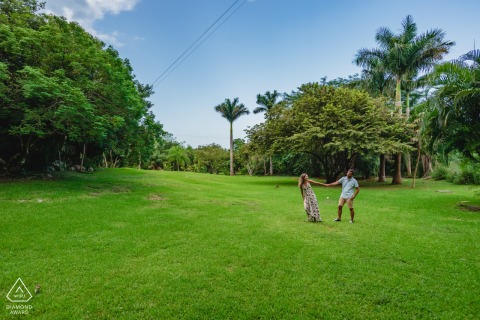 This portrait in the fields of a Valladolid, Mexico hacienda captures the couple holding hands while walking through a lush green pasture, with palm trees in the background.