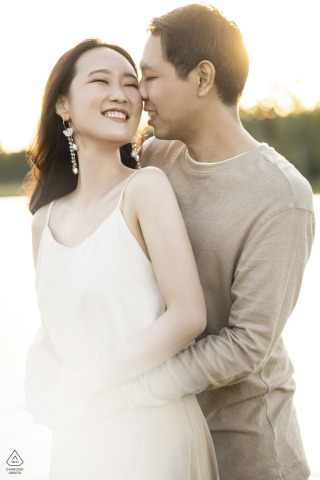 In Khao Yai, Thailand, a couple image captures him standing behind her, sunlight softly illuminating them as she smiles brightly in the washed-out light.