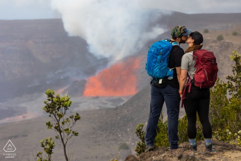 This portrait from Hawaii Volcanoes National Park captures the couple smooching in celebration of seeing the volcano erupt dramatically from the rim, marking an unforgettable experience.