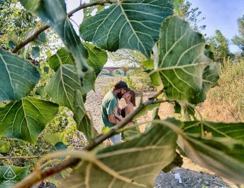 At Fiume Vara in Ceparana, a couple shares a kiss framed by lush vining foliage, highlighting their natural love in the Italian landscape.