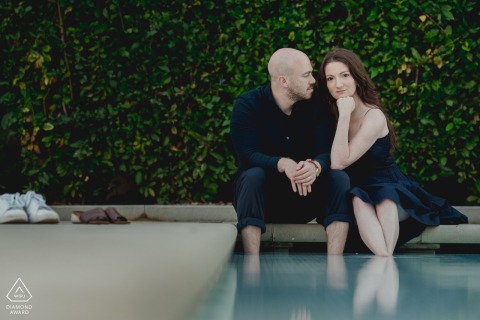 This romantic Tuscany couple portrait at Castello del Nero, Firenze, shows the pair sitting close on the edge of a pool with their feet in the water; she looks at the camera while he gazes at her.