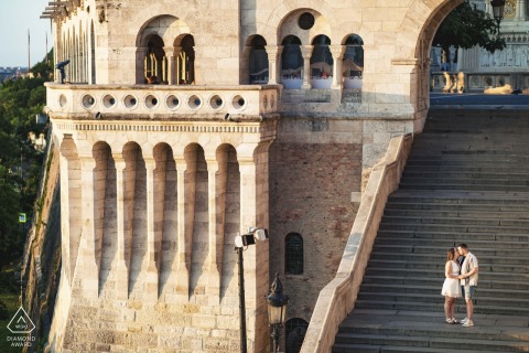 Golden Light on Castle Steps in Budapest Couple Portrait Session In Budapest's golden light, the couple stands on the massive stairs of an old world stone castle, a stunning portrait that captures their love and the city's majesty.