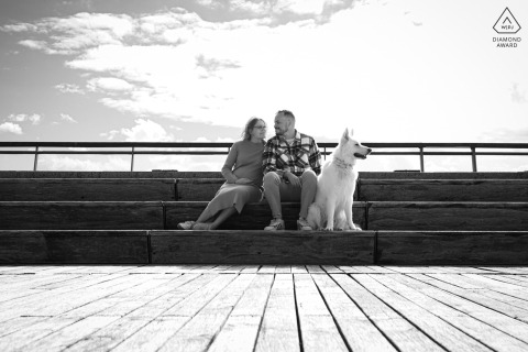 Near Mont Saint Michel, a couple relaxes together, framed in a symmetrical black-and-white shot from a low angle, with leading lines in the deck boards below guiding the eye.