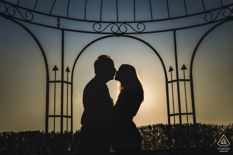 At Fonteverde Resort in Tuscany, a couple is photographed face to face in profile, silhouetted under iron trellis work at sunset and about to share a kiss.