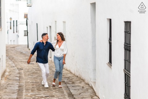 In Vejer de la Frontera, Cádiz, Spain, a pre-wedding portrait captures the couple walking quickly, arms around each other, with purposeful steps through the village alley.