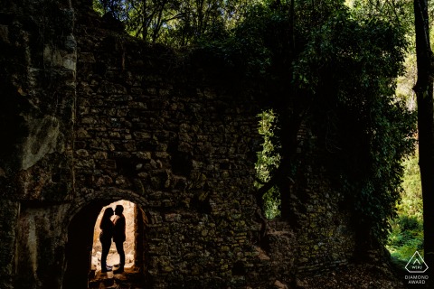 At Baños de Popea, Córdoba, Spain, a pre-wedding portrait captures the couple head to head, holding each other in silhouette within a lit doorway.