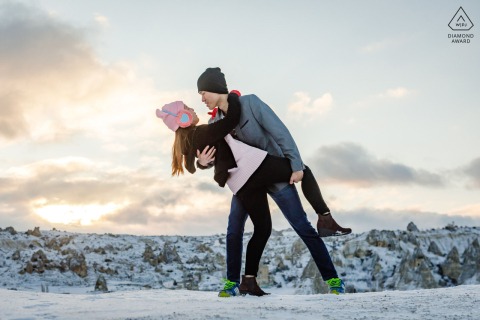 In Göreme, Nevşehir, Turkey, a Cappadocia pre-wedding photo session captures the couple playing in the snow, wearing beanies, sharing a playful and romantic dip.