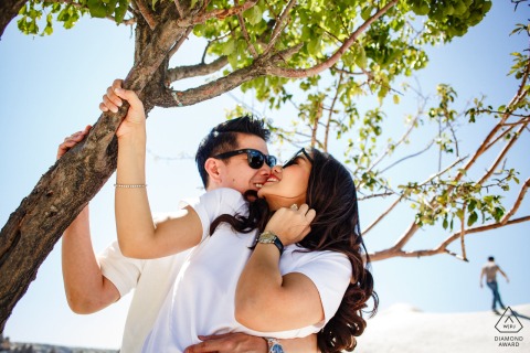 In Göreme, Nevşehir, Turkey, a Cappadocia pre-wedding photo features the couple holding the trunk of a small tree, nestling their faces together and smiling on a sunny day.
