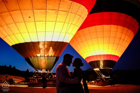 In Göreme, Nevşehir, Turkey, a Cappadocia pre-wedding portrait features the couple face to face in profile silhouettes, with colorful hot air balloons filling the frame at sunrise.