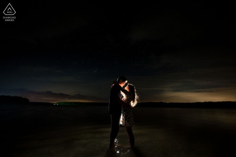 Engaged Couple Under Night Sky by Water in Doylestown Portrait Session In Doylestown, Philadelphia, two hearts meet between the stars and the water, illuminated under the night’s gentle glow by the photographer’s artful lighting.