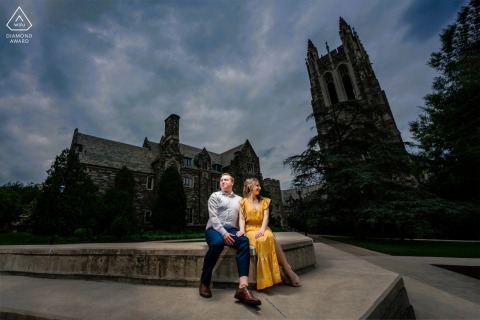 Engaged Couple at Dusk by Historic Stone Building in Philadelphia In Philadelphia, Pennsylvania, a couple is seated together against the backdrop of a historic stone building and dramatic skies, beautifully illuminated in a dusk portrait.