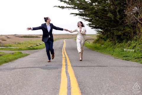 Engaged Couple Running Down the Street at Cypress Grove in Mendocino At Cypress Grove in Mendocino, CA, the couple joyfully runs down the center of the street, the yellow painted lines leading the eye straight toward their laughter and energy.