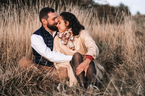 At Chapelle Saint-Aubin in France, the couple sits close together in tall, dry grass, embracing with eyes closed, conveying intimacy and peaceful connection.