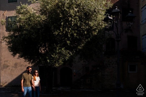 Engaged Couple Walking in Sunlight and Shadow During Portrait Session in Grado In Grado, Gorizia, Italy, the couple walks together in sunlight, with dramatic shadows filling the right side of the frame and warm light illuminating them.