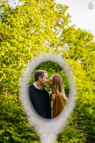 In the Catskills, NY, the couple enjoys each other's company in the woods, their smiling reflection captured in a handheld mirror framed by lush green foliage.