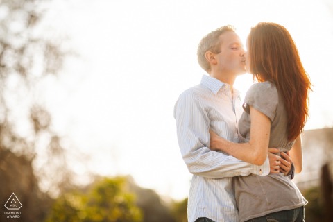 In San Francisco, CA, an engagement portrait captures the couple face to face, sharing a kiss as bright sunlight from behind washes out the scene in a dreamy glow.