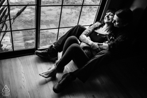 In San Jose, CA, an engagement portrait captures the couple cozily cuddling indoors by a floor-to-ceiling window, lying back together in a relaxed embrace.
