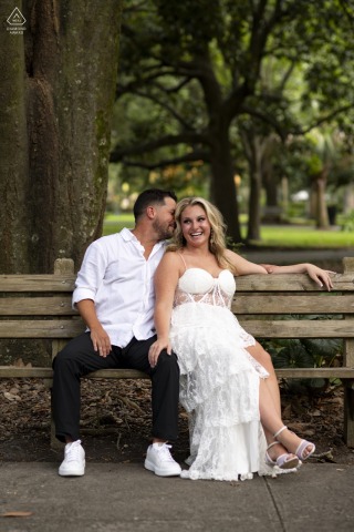 At Forsyth Park in Savannah, Georgia, a couple sits together on a small wooden bench for their portrait.