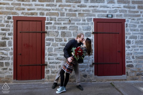 In Old Montreal, Quebec, Canada, a couple poses in a dip and kiss between two red doors on a stone back alley wall of a 20th-century building for their portrait.