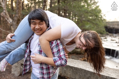 At Vaughn Woods in Hallowell, Maine, a man playfully lifts his partner over his shoulder as they both laugh for a lighthearted portrait.