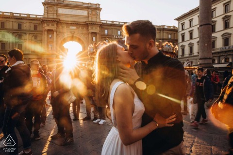 In Florence, Italy, a couple stands together in a crowd with sunlight bursting from behind for their portrait.