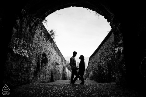 In Grenoble, France, a couple is silhouetted in black and white beneath the stone arch of an old-world building for a portrait.